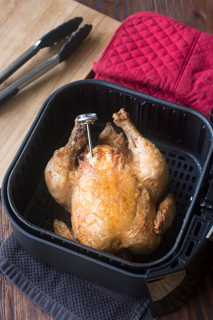 Whole roasted chicken in an air fryer basket, with a meat thermometer.