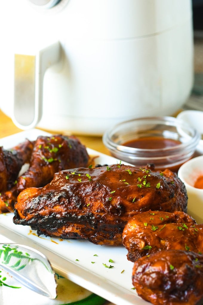 BBQ Chicken on a white rectangular platter, with dish of more BBQ sauce in background.