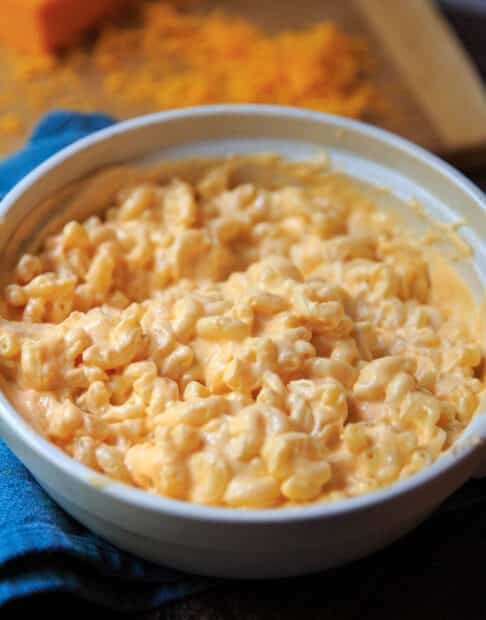 Serving dish of creamiest mac and cheese with grated cheddar in background.