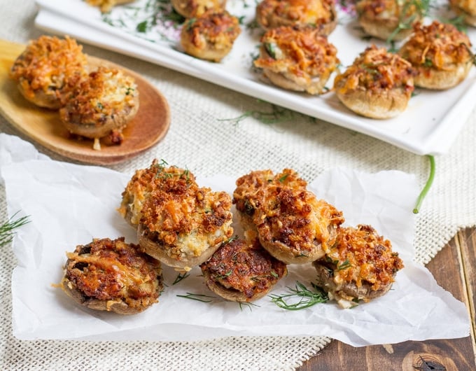 Little stuffed mushrooms on a white platter and parchment paper.