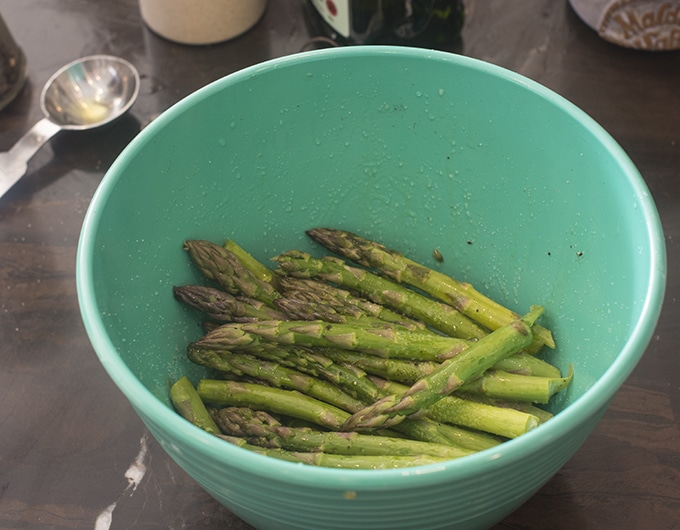 Seasoned, raw asparagus in a blue bowl.