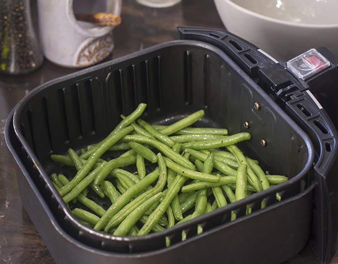 Uncooked green beans in air fryer basket.