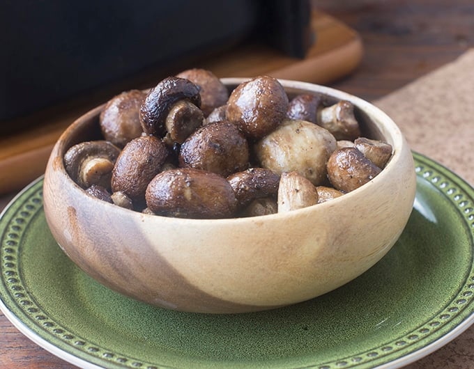 Brown bowl of cooked whole mushrooms sitting on a green plate.