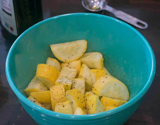 Raw cut yellow squash seasoned in a blue bowl.