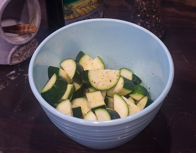 Sliced and seasoned zucchini in light blue bowl.
