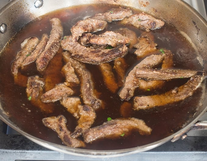 Cooked beef strips in beef stock  in pan.