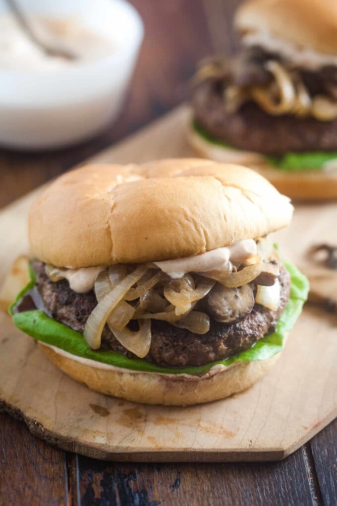 A burger with mushrooms and onions and lettuce on it.