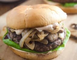 A burger with mushrooms and onions and lettuce on it.