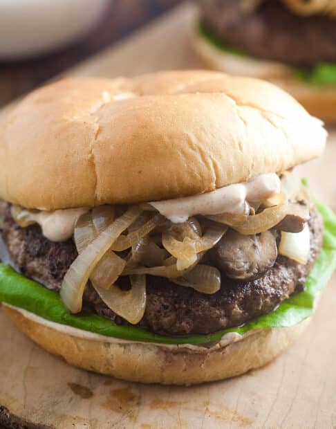 A burger with mushrooms and onions and lettuce on it.