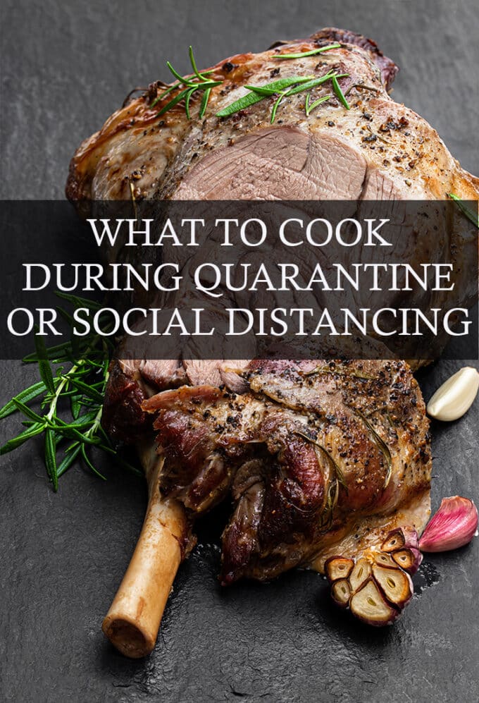 Bone-In Roast garnished with rosemary leaves sitting on a black slate surface; garlic cloves and rosemary sprigs are scattered around the roast; the text overlay reads, "What To Cook During Quarantine Or Social Distancing".