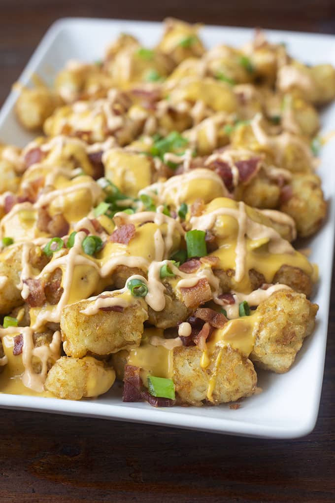 Super Tots is the most craveable appetizer recipe. It's topped with queso, bacon, green onion, and sriracha mayo to add some spice.