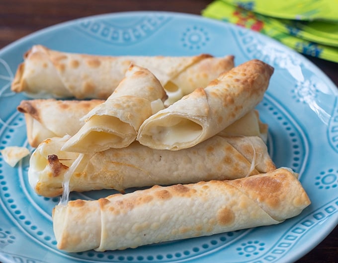 mozzarella sticks in egg roll wrappers on light blue bpalte