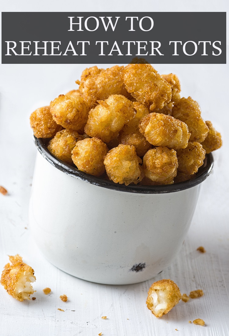 white enameled metal bowl with black rim piled high with golden tater tots; text overlay across the top reads, "How To Reheat Tater Tots"