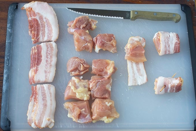 Raw bacon and chicken pieces on plastic cutting board.
