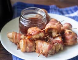 Bacon wrapped chicken bites on a white plate with a dipping sauce.