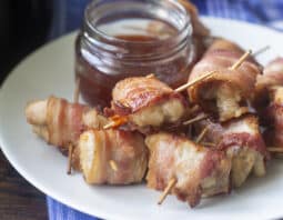 Bacon wrapped chicken bites on a white plate with a dipping sauce.