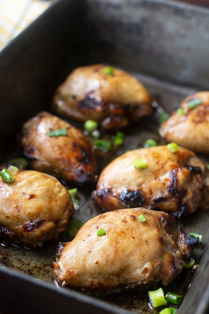 baked chicken thighs in metal baking pan with green onion garnish