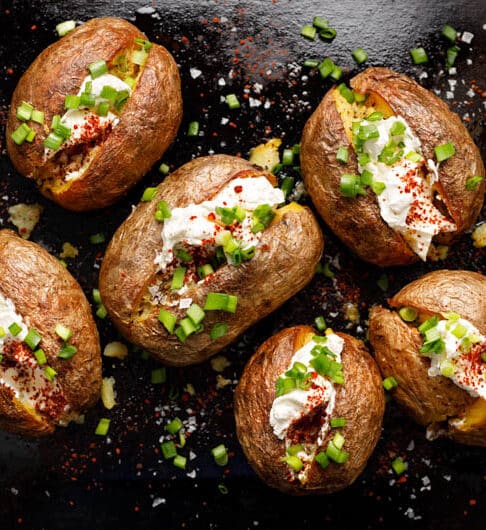 6 baked potatoes on baking tray with cream cheese, chives, and kosher salt