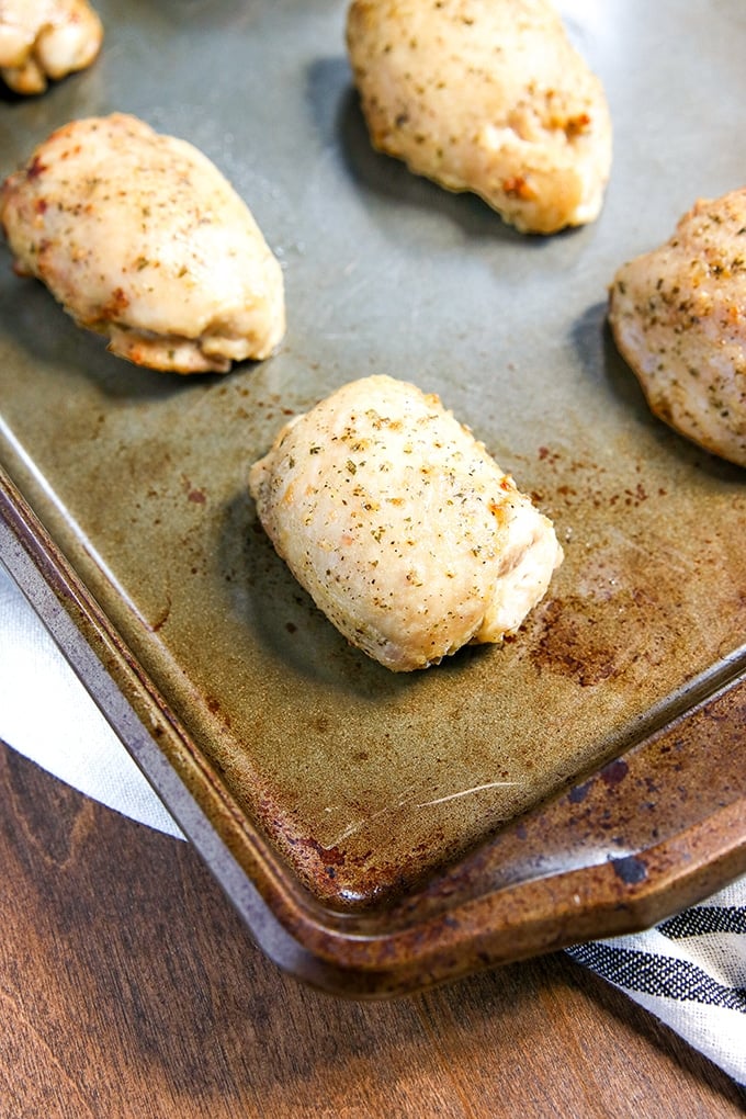 sheet pan with 4 chicken thighs seasoned with ranch seasoning on it; white cloth with black stripe under pan