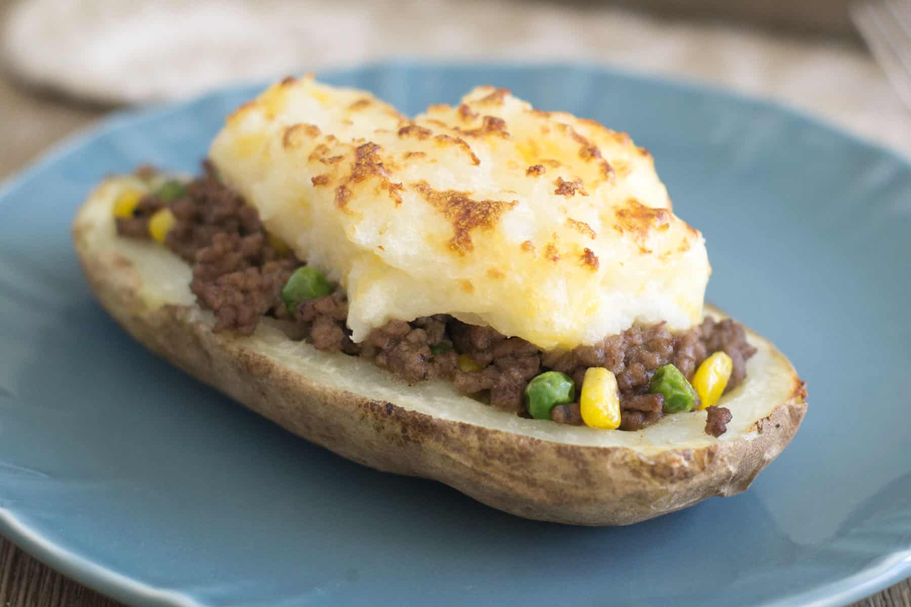 A half of a potato filled with a ground beef and veggie mixture and topped with broiled mashed potatoes