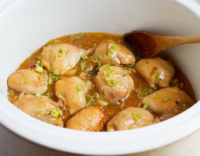 8 chicken thighs in white crock with chopped green onion on top in a light brown broth; wooden spoon in crock