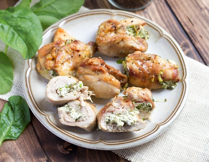 6 chicken thighs stuffed with cream cheese and spinach lightly browned with black pepper on top; on gray'ish colored plate with brown striped rim; on white cloth; spinach leaves in background and salt and pepper in background