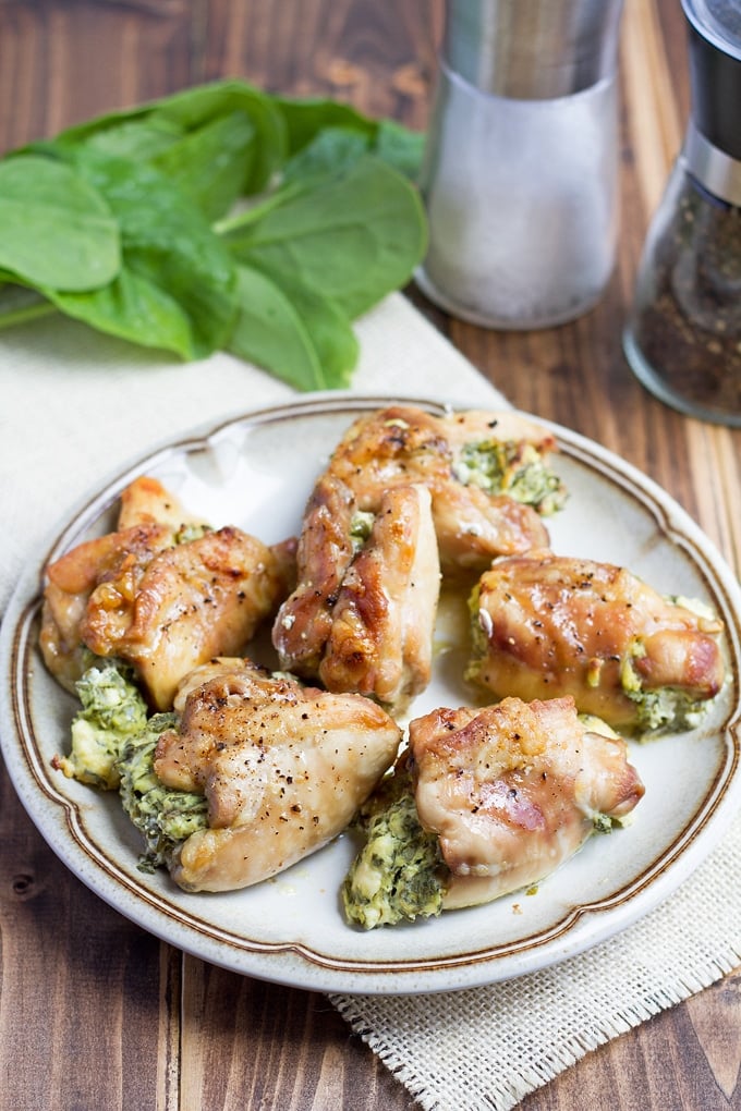 6 chicken thighs stuffed with cream cheese and spinach lightly browned with black pepper on top; on gray'ish colored plate with brown striped rim; on white cloth; spinach leaves in background and salt and pepper in background