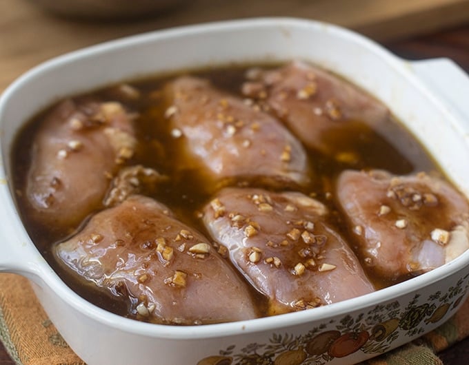 chicken thighs in small white casserole dish with handles; sitting in brown marinade liquid with minced garlic