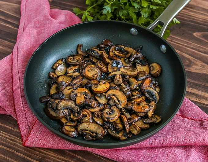 frying pan with sliced sauteed mushrooms with bright pink cloth underneath; parsley in background