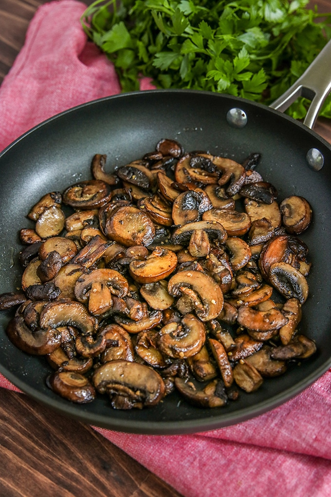 frying pan with sliced sauteed mushrooms with bright pink cloth underneath; parsley in background