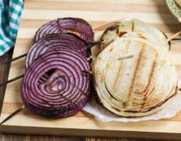 Skewered slices of grilled red and vidalia onion on a plate.