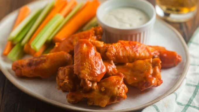 buffalo wings on white plate with carrot and celery sticks and dip in small white bowl