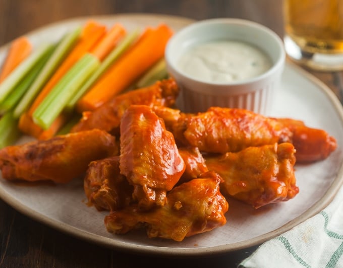 buffalo wings on white plate with carrot and celery sticks and dip in small white bowl