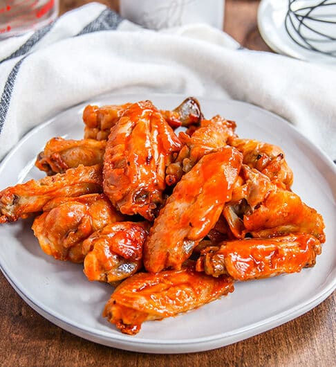 buffalo chicken wings on a white plate; white cloth with blue stripes in background