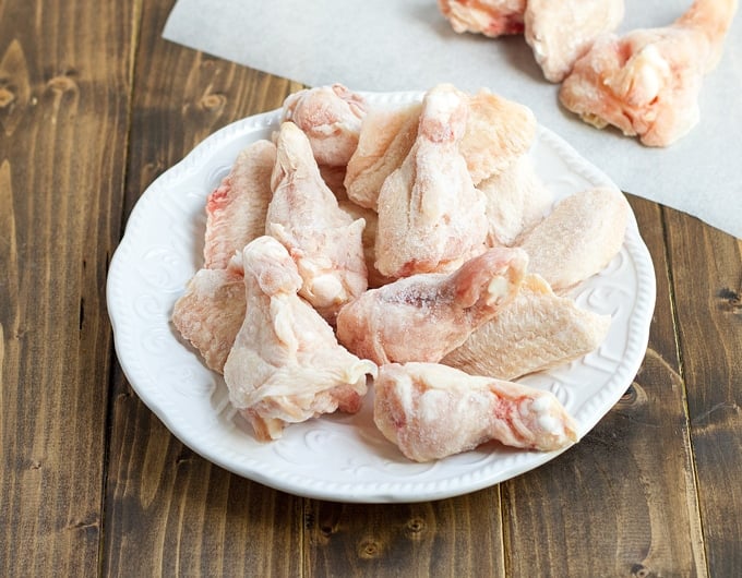 frozen chicken on white plate with cutting board in background