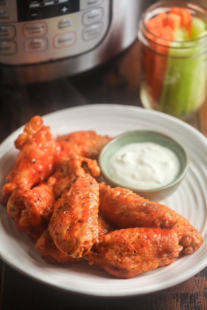 Instant Pot Chicken Wings Buffalo wings on a white plate with blue cheese dressing; jar with carrot and celery stick in jar in background and instant pot