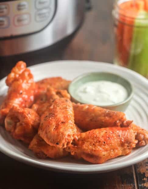 Buffalo chicken wings on a plate with ranch. in front of Instant Pot.