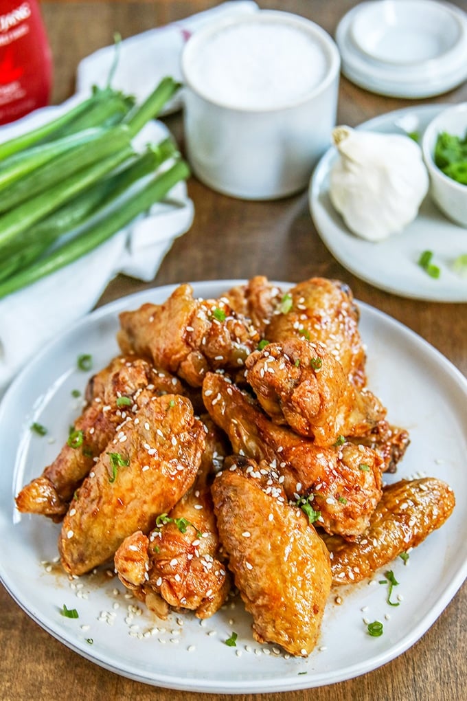 fried wings garnished with chive and sesame seeds on light gray plate; small condiment plate in background with garlic and chives on it; bunch of green onions in background