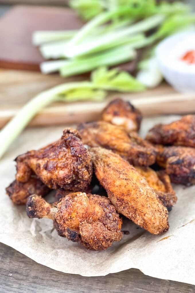 Crispy chicken wings with dry rub on parchment with celery in background.