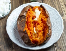 baked sweet potato cut open with butter on a white plate