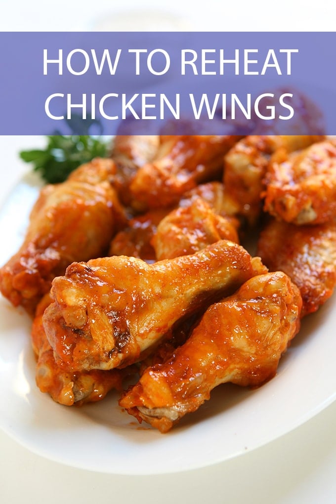 white plate with chicken wings tossed in a red sauce. A sprig of parsley is garnishing the plate. Across the top of the picture reads, "How To Reheat Chicken Wings".