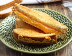 green plate with grilled cheese with orange melty cheese; stack of white bread in background; plaid cloth and air fryer