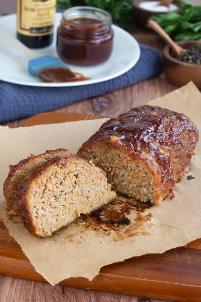 Sliced turkey meatloaf with BBQ sauce on parchment paper with more sauce in background.