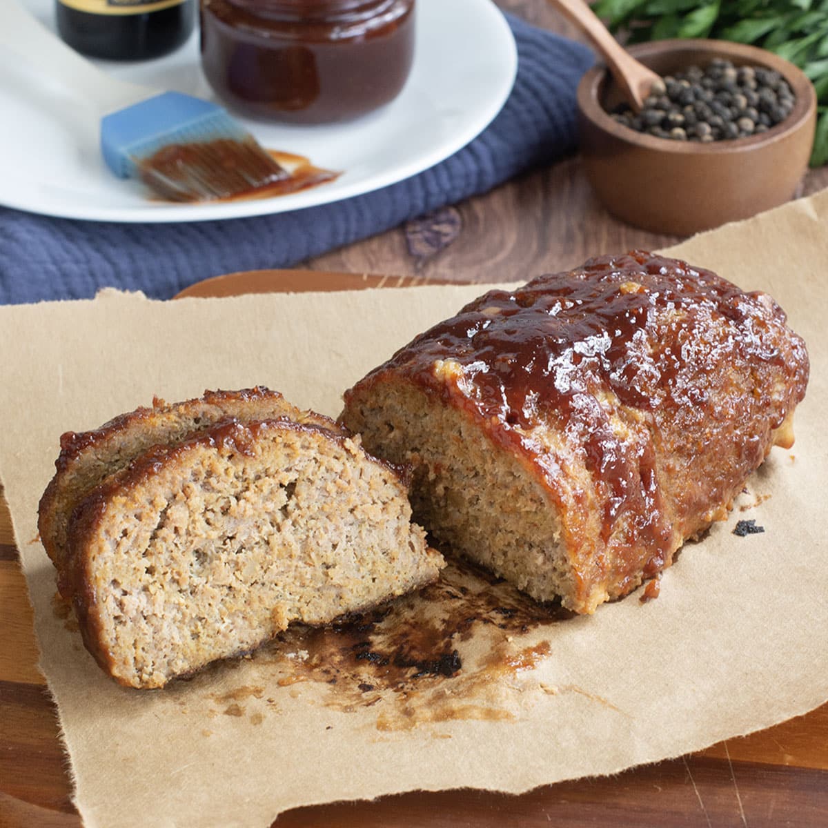 Sliced turkey meatloaf with BBQ sauce on parchment paper with more sauce in background.