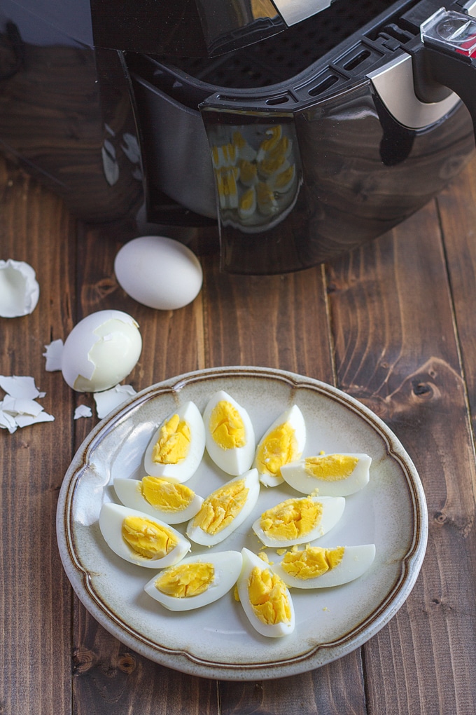 tan plate with brown line around edge with quartered hard boiled eggs on plate; air fryer in background as well as whole hard boiled egg with broken shell