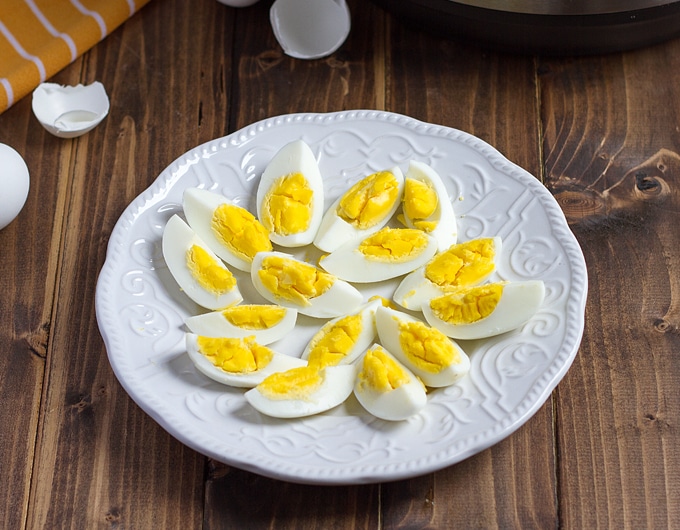 white plate with quartered hard boiled eggs on it; with shells in background and orange striped cloth