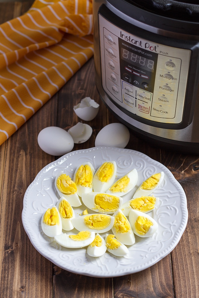 white plate with quartered hard boiled eggs on it; with shells in background and orange striped cloth; instant pot in background