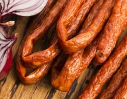 Pepperoni sticks close-up with a halved red onion.