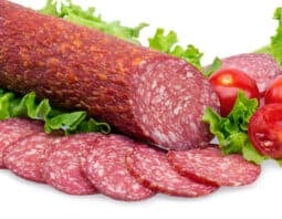 A chunk of salami on a white background with some slices cut from it.