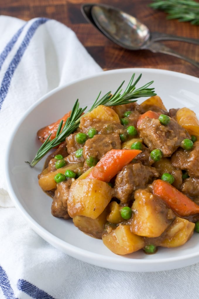 lamb, potato, carrots, peas in a white bowl with sprig of rosemary